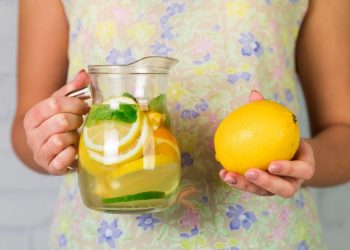 Woman holding lemon and pitcher of citrus water