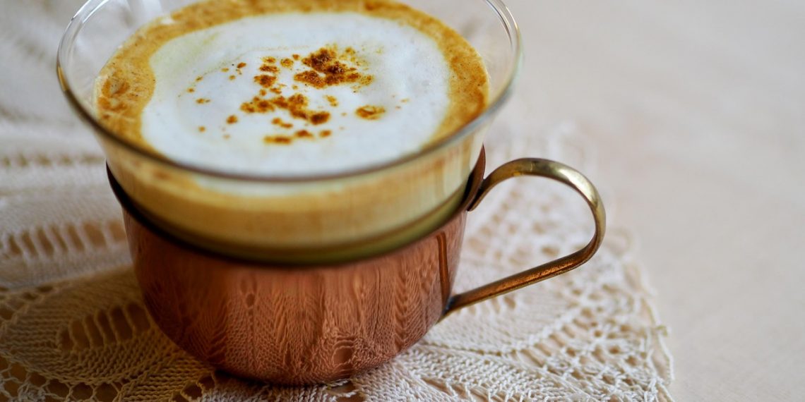 Creamy latte topped with cinnamon in a copper cup on lace {focus_keyword}.