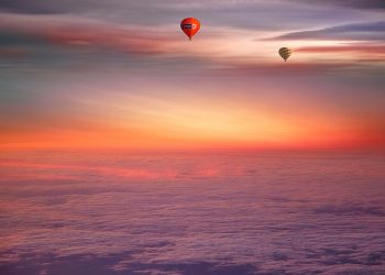 Two hot air balloons floating under a colorful sunset sky.