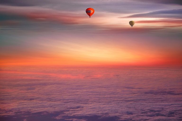 Two hot air balloons floating under a colorful sunset sky.