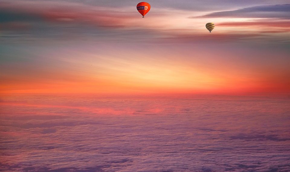 Two hot air balloons floating under a colorful sunset sky.