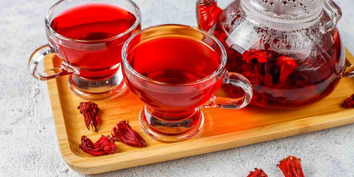 Two cups and a teapot of hibiscus tea on a wooden tray.