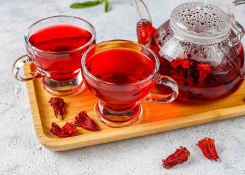 Two cups and a teapot of hibiscus tea on a wooden tray.