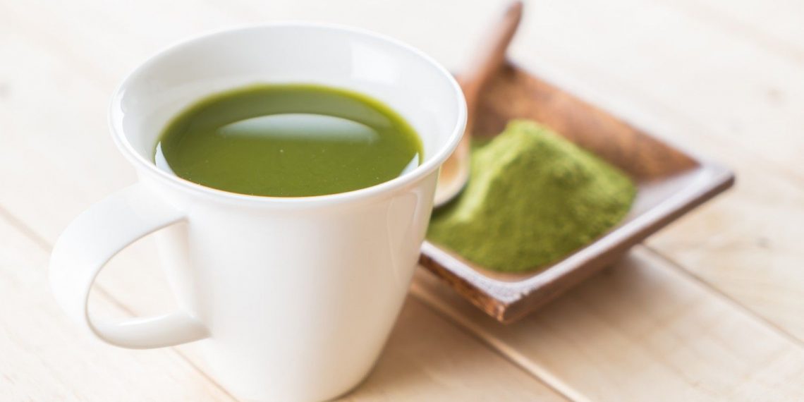 Cup of green matcha tea with powder on wooden table.