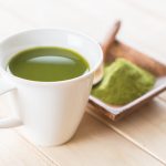 Cup of green matcha tea with powder on wooden table.