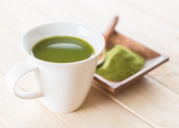 Cup of green matcha tea with powder on wooden table.