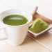 Cup of green matcha tea with powder on wooden table.