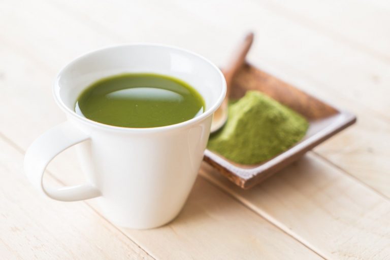 Cup of green matcha tea with powder on wooden table.