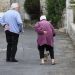 Elderly couple walking with a small dog on a village street.