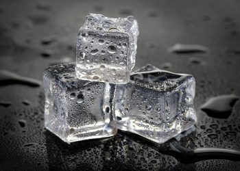 Three stacked ice cubes on wet surface with droplets.