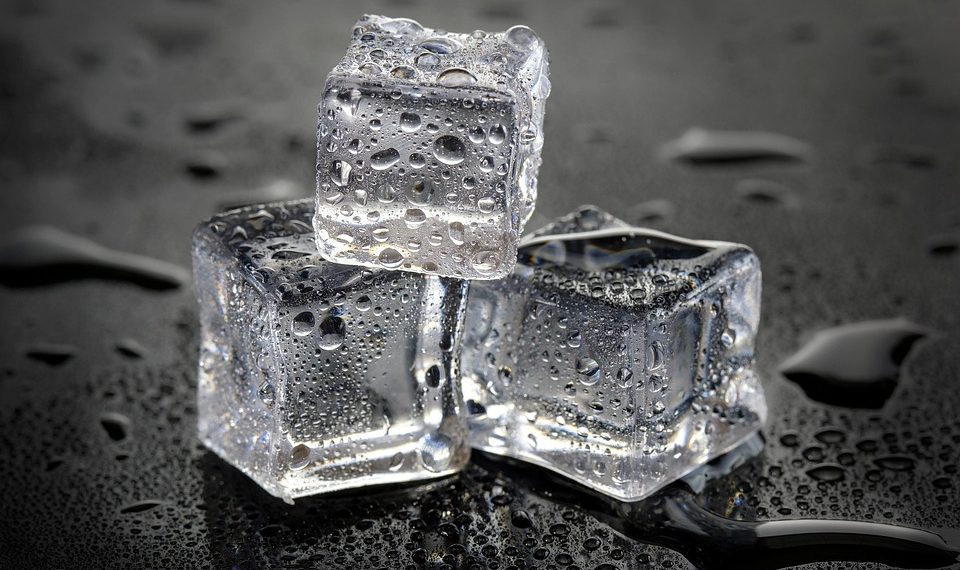 Three stacked ice cubes on wet surface with droplets.