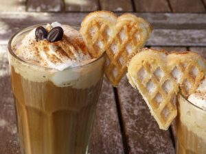 Cinnamon-topped latte with whipped cream and heart-shaped waffles.