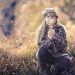 Girl in hat blowing dandelion seeds in a field.