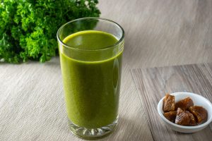 Green smoothie with parsley and figs on a wooden table.