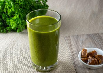 Green smoothie with parsley and figs on a wooden table.