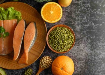 Fresh salmon with orange slices and mung beans on a wooden platter.