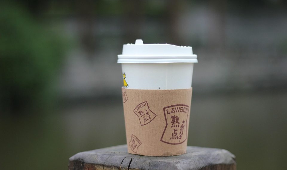 Cup of coffee on wooden post outdoors.