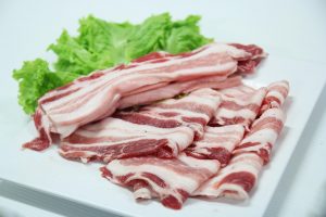 Sliced uncooked pork belly with lettuce on a plate.