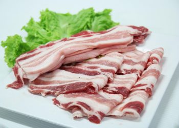Sliced uncooked pork belly with lettuce on a plate.