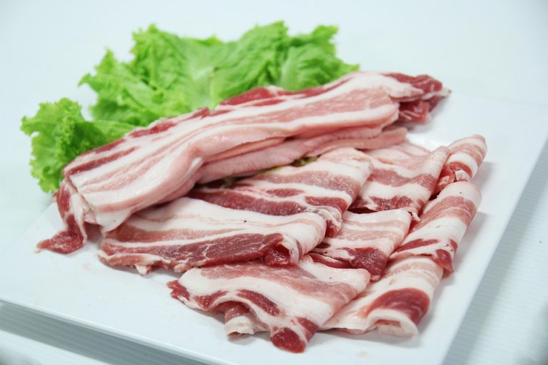 Sliced uncooked pork belly with lettuce on a plate.