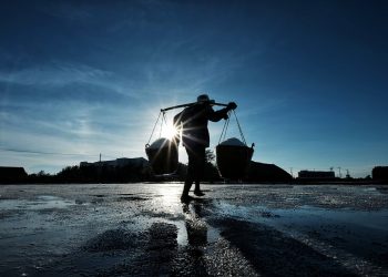 Silhouetted worker carrying baskets at sunrise.