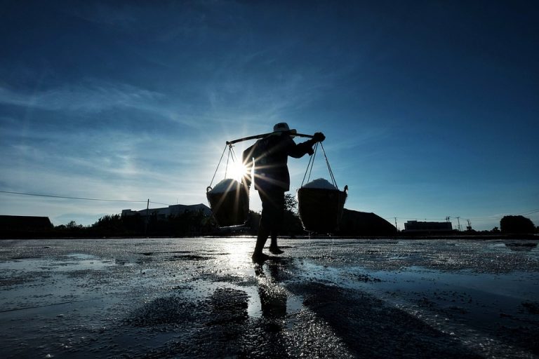 Silhouetted worker carrying baskets at sunrise.