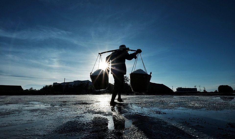 Silhouetted worker carrying baskets at sunrise.