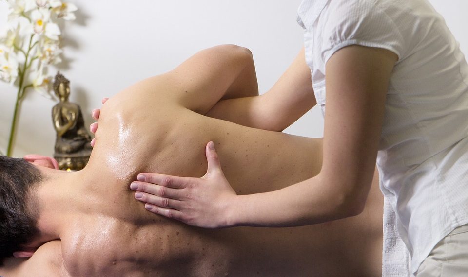 Massage therapist applying oil on a client's back during a treatment.