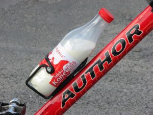 Bottle of milk secured on a red bicycle frame.