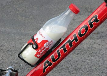 Bottle of milk secured on a red bicycle frame.