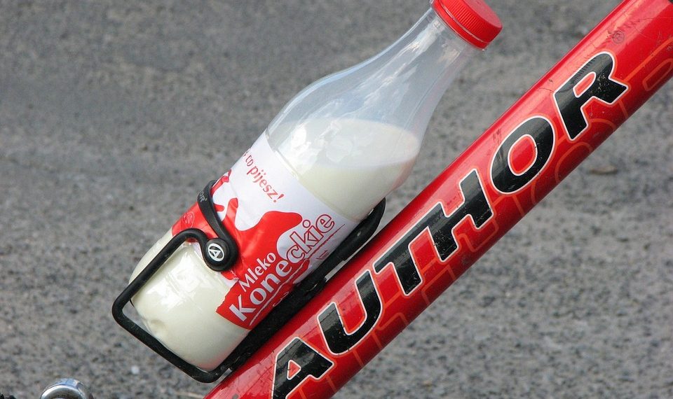 Bottle of milk secured on a red bicycle frame.