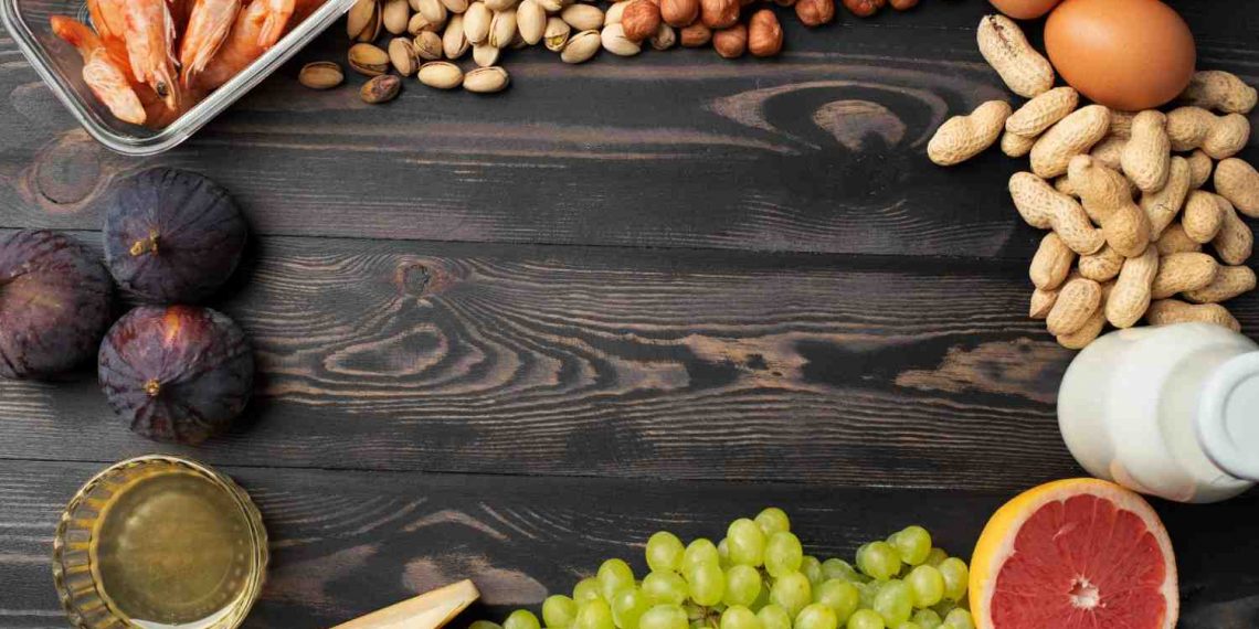 Assorted foods on wooden table, including shrimp, nuts, eggs, figs, and grapefruit.