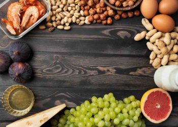 Assorted foods on wooden table, including shrimp, nuts, eggs, figs, and grapefruit.