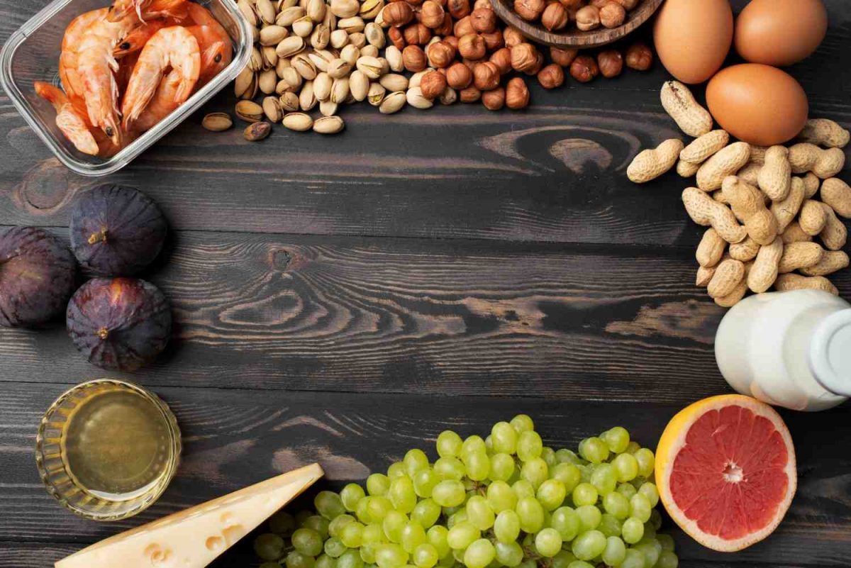Assorted foods on wooden table, including shrimp, nuts, eggs, figs, and grapefruit.