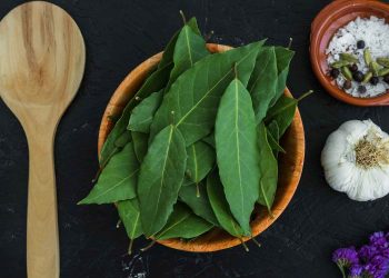 Bay leaves in a wooden bowl next to garlic and spices.