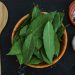 Bay leaves in a wooden bowl next to garlic and spices.