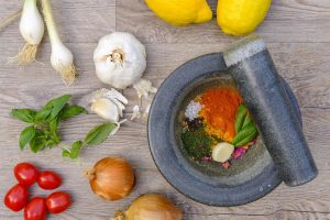 Fresh ingredients and spices with mortar and pestle on wooden surface.