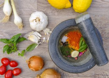 Fresh ingredients and spices with mortar and pestle on wooden surface.