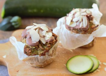 Zucchini muffins topped with almond slices next to fresh zucchini slices.