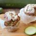 Zucchini muffins topped with almond slices next to fresh zucchini slices.