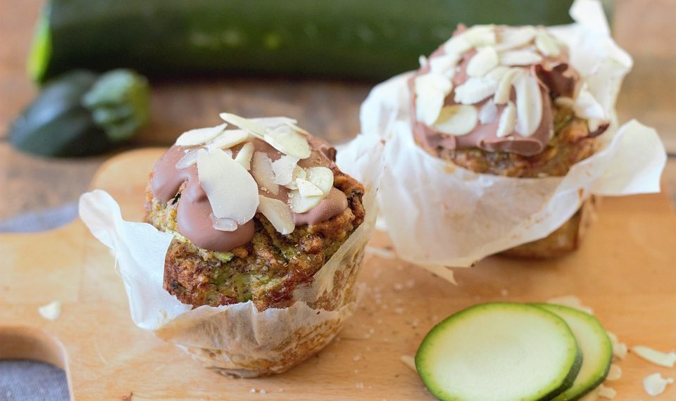 Zucchini muffins topped with almond slices next to fresh zucchini slices.
