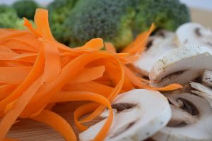 Sliced mushrooms and carrot ribbons with broccoli in background.