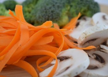 Sliced mushrooms and carrot ribbons with broccoli in background.
