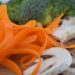 Sliced mushrooms and carrot ribbons with broccoli in background.