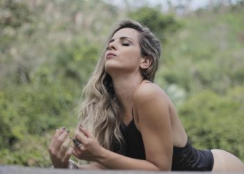 Woman relaxing outdoors with serene expression, lush greenery background.