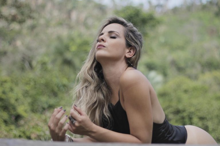 Woman relaxing outdoors with serene expression, lush greenery background.