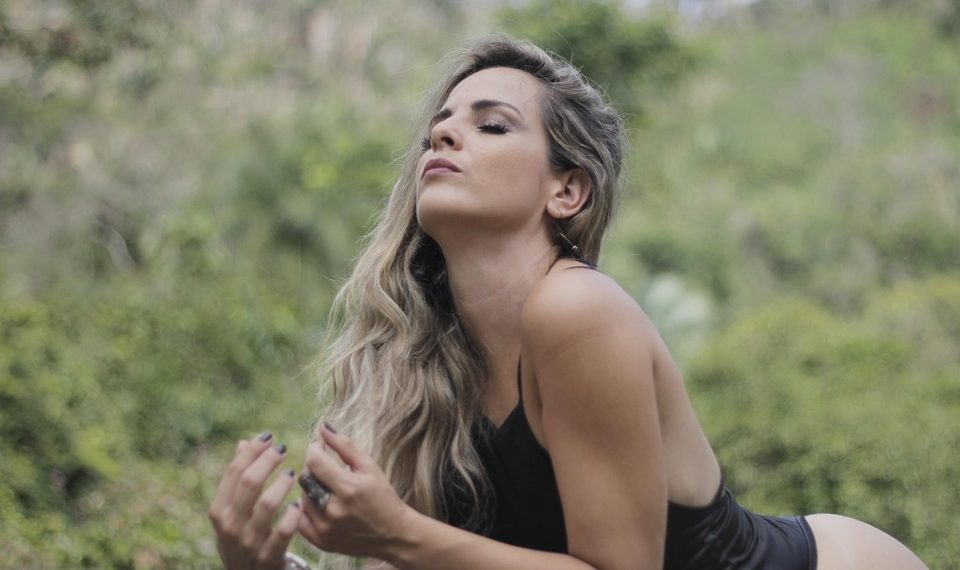 Woman relaxing outdoors with serene expression, lush greenery background.