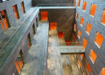 Modern atrium with orange accents and glass walkways, showcasing stylish architecture.