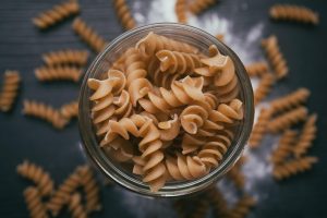 Whole wheat spiral pasta in a glass jar on a wooden table.