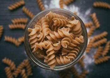 Whole wheat spiral pasta in a glass jar on a wooden table.